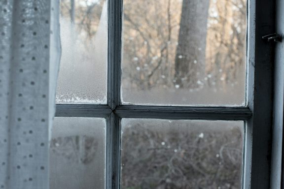 Frostbedeckte Fensterscheibe mit verschwommenem Blick auf die winterliche Landschaft.